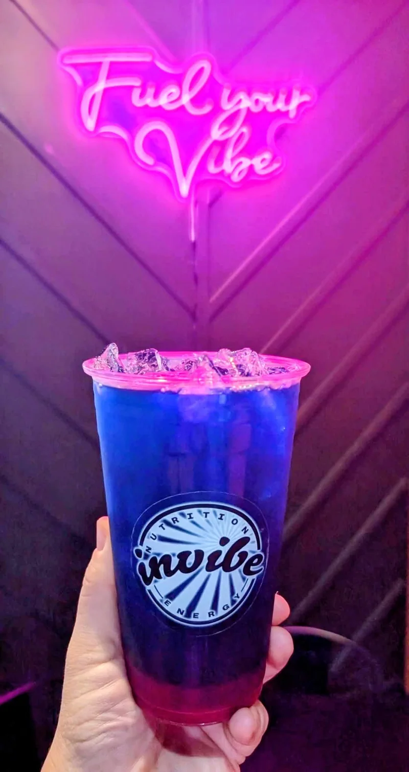 A layered blue and purple InVibe tea beneath the pink Fuel Your Vibe neon sign