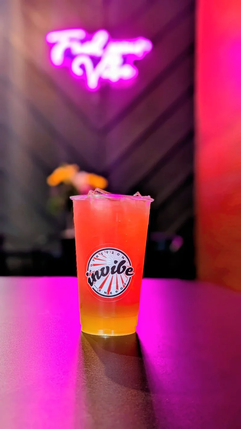 An orange and yellow InVibe tea on the pink table beneath the club neon sign