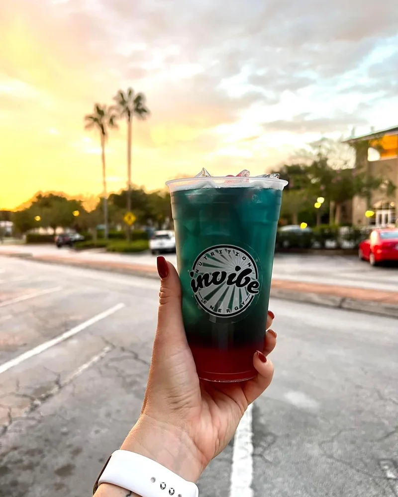 A hand holding a colorful InVibe tea outdoors at sunset